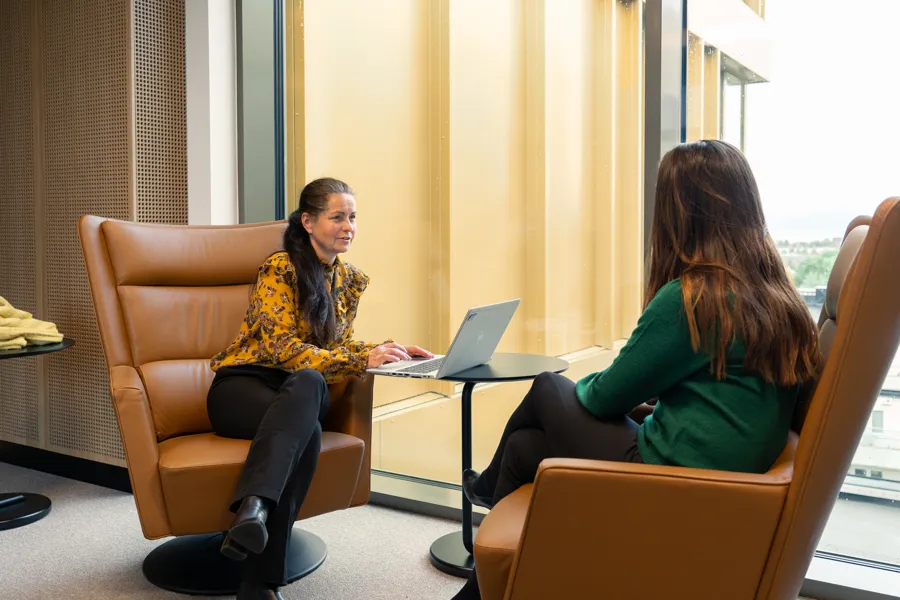 Kvinner sitter med PC i lenestoler og prater