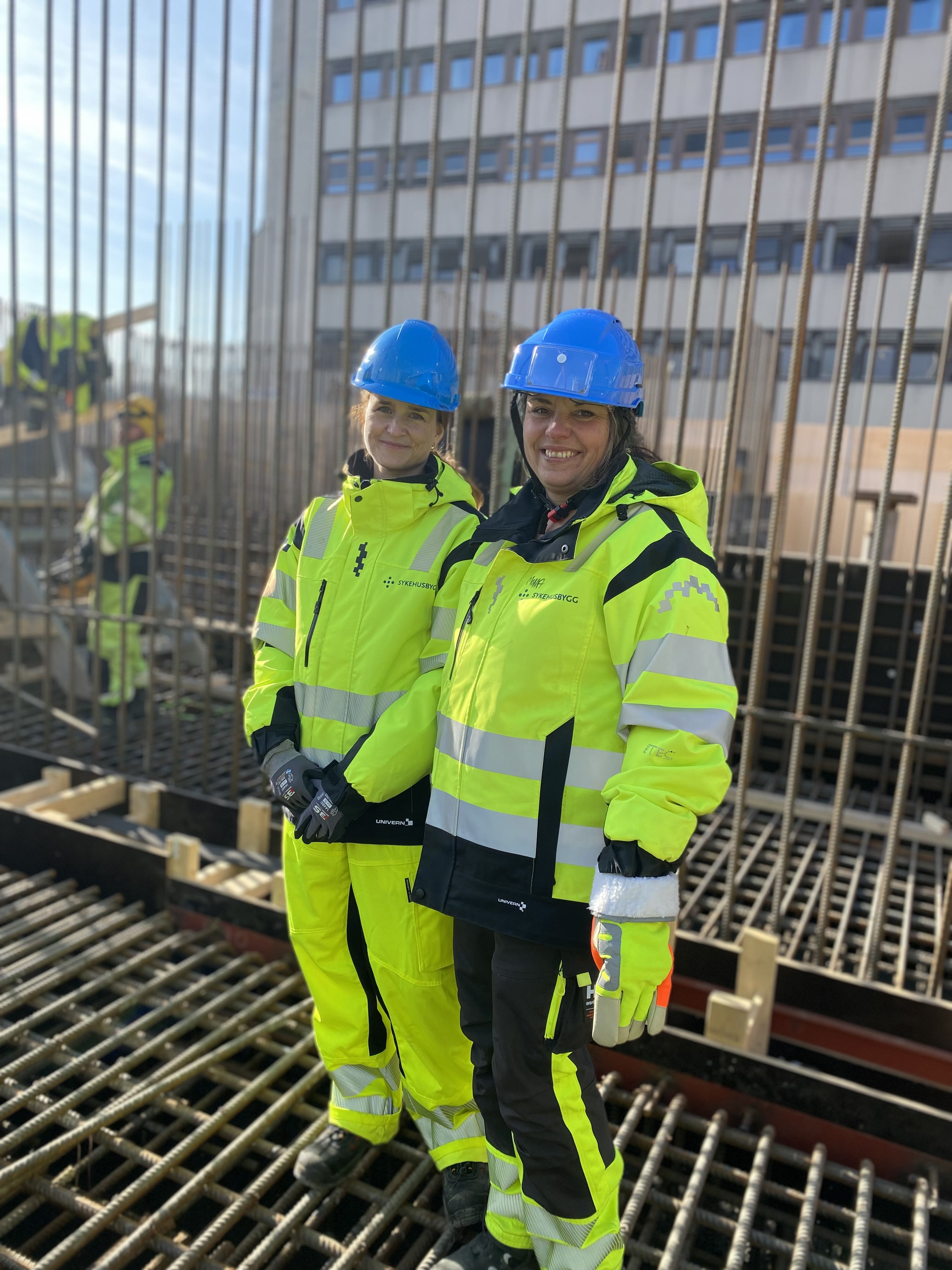 Et par menn iført hjelm og stående på en metallramme