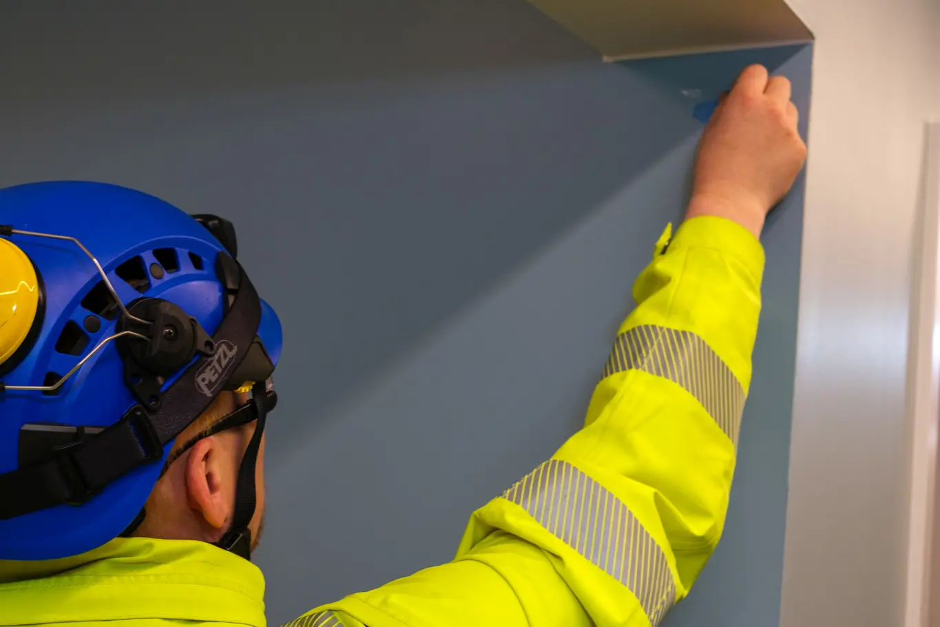 En mann iført hjelm og gul jakke som holder en hvit vegg