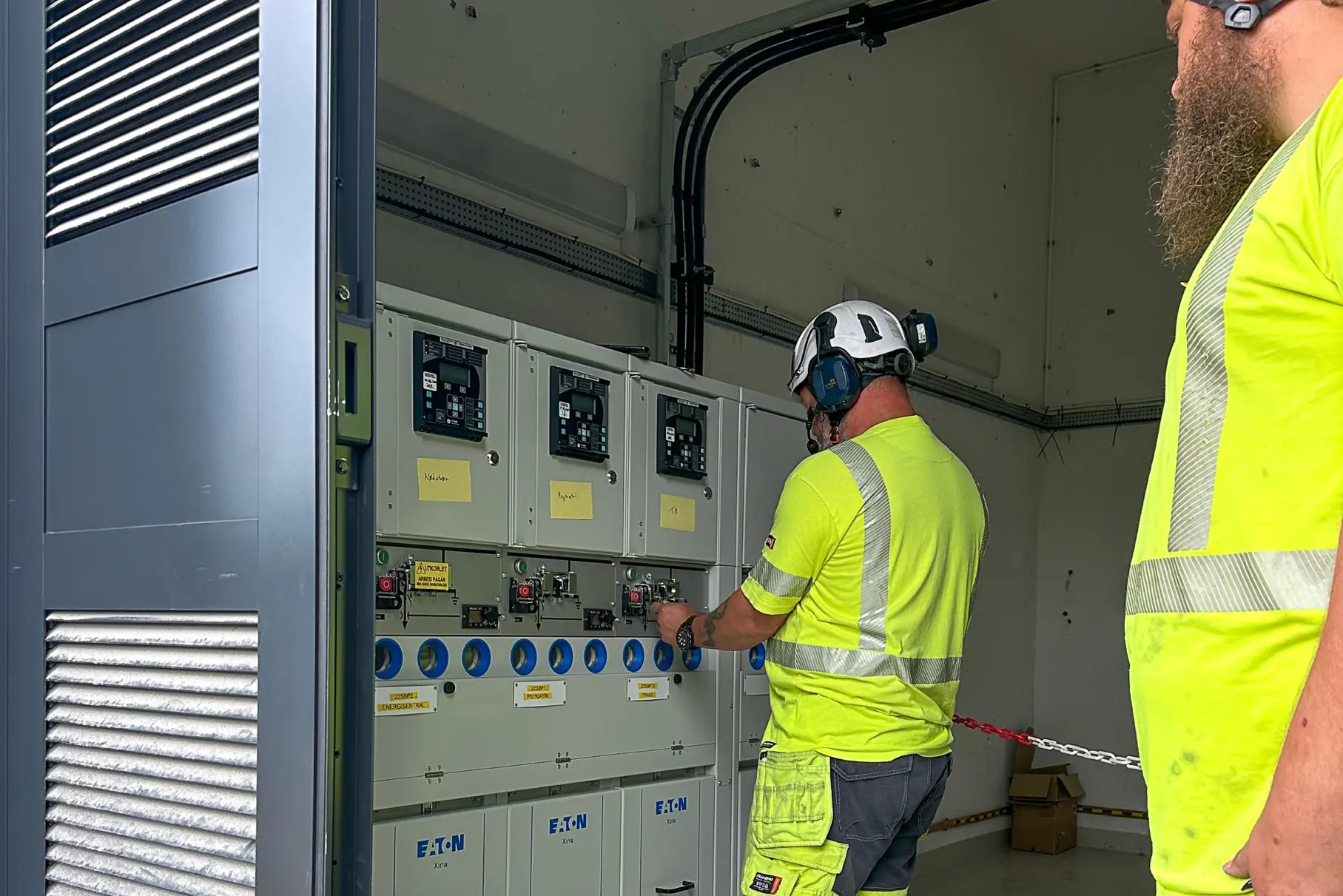 Noen få menn i sikkerhetsvester som jobber på en maskin